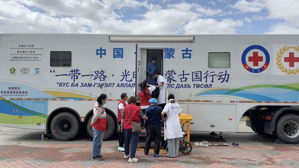 医护人员与红十字志愿者共同搀扶蒙古国白内障患者登上流动复明手术车。